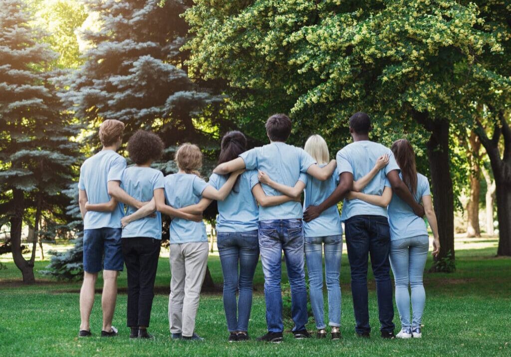 Volunteering, people and ecology concept. Group of volunteers embracing in park, back view, copy space